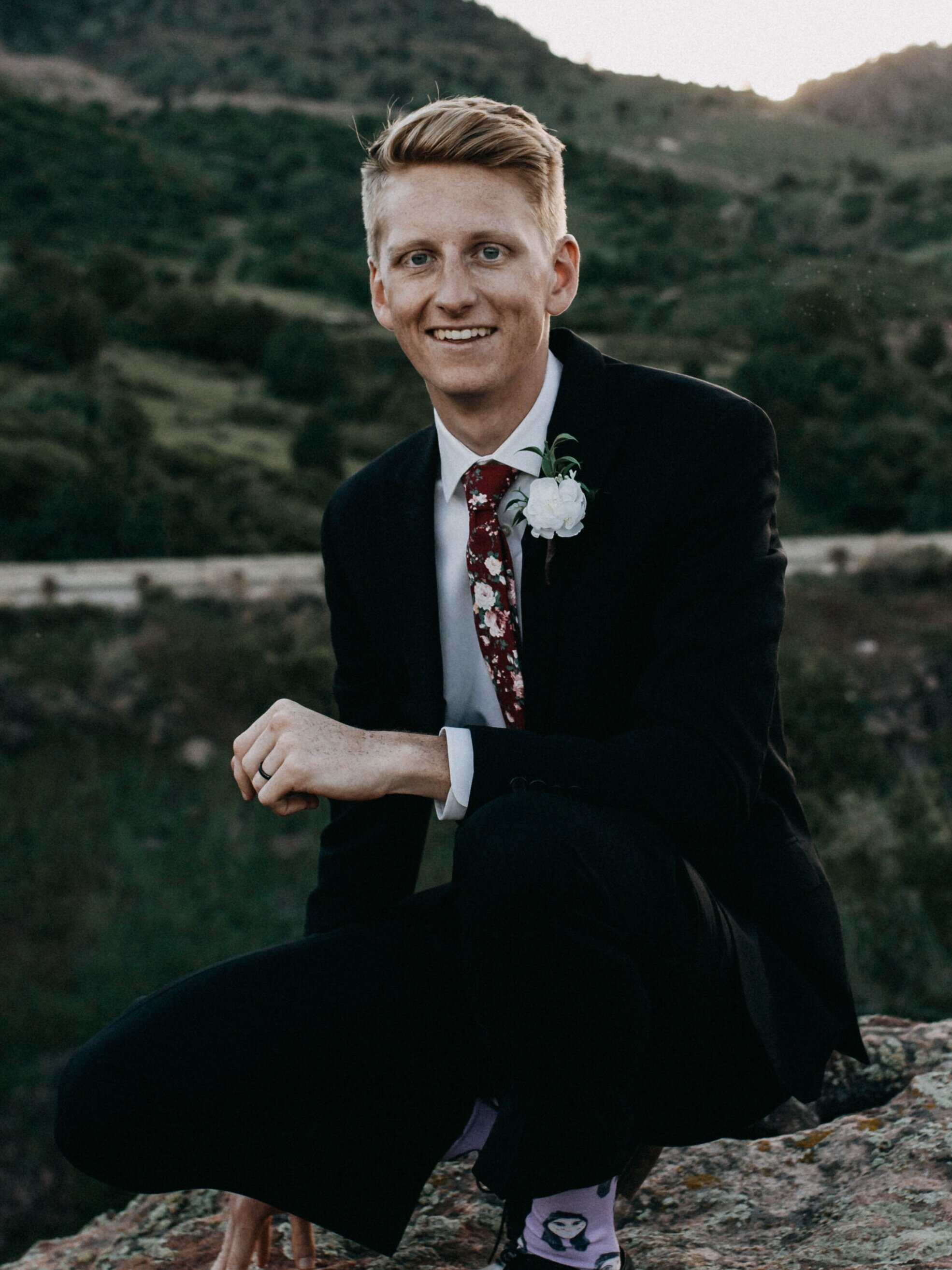 Daniel Lindeen in a suit, crouched on a rock in the hills